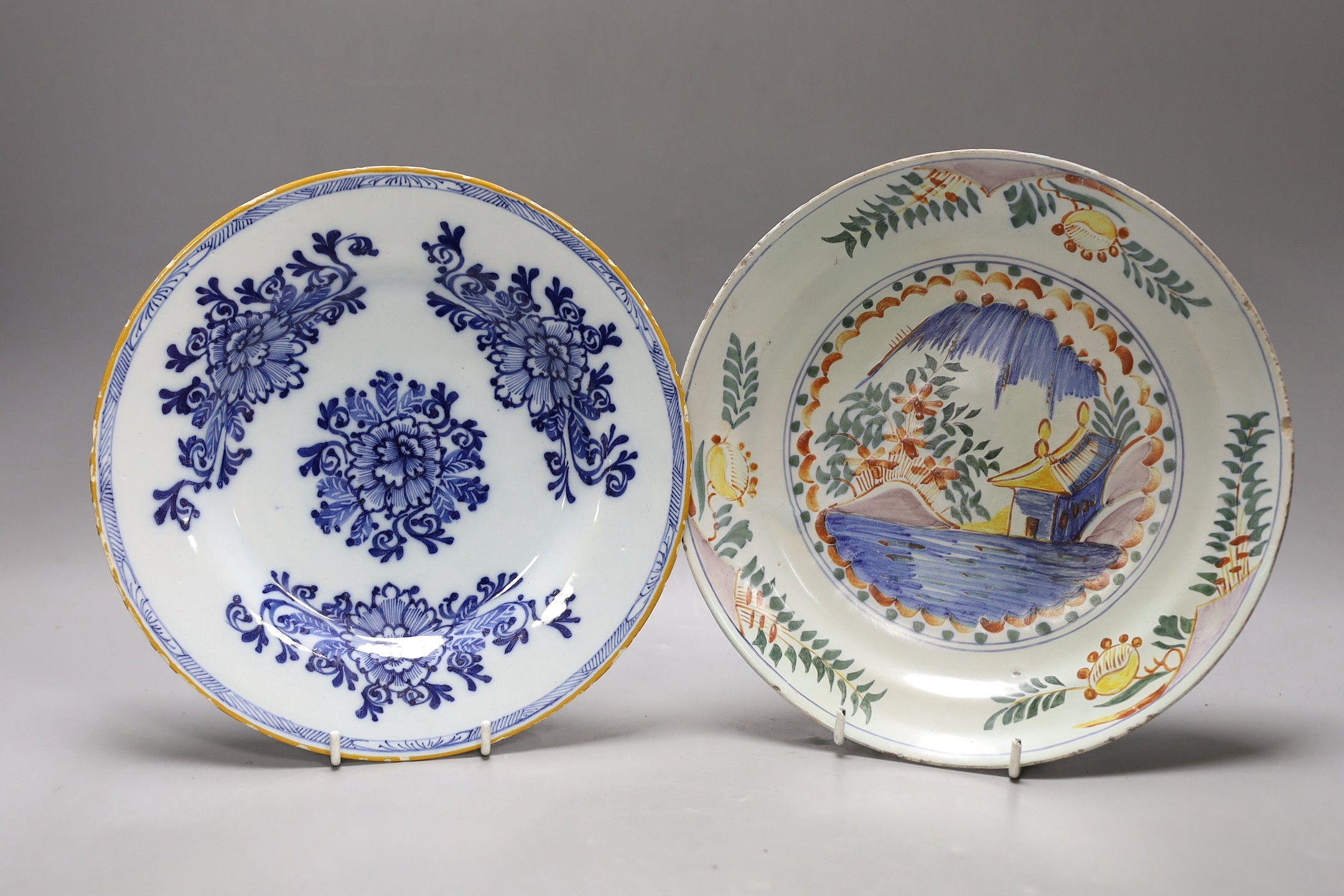 An early 18th century Delft polychrome dish and a mid 18th century Delft blue and white plate, largest 23.5cm diameter